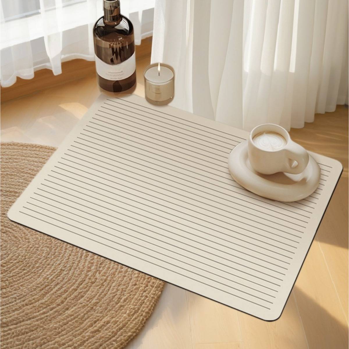 Cremefarbene gestreifte Matte auf einem sonnenbeschienenen Holzboden neben einem gewebten Teppich, mit einer Kaffeetasse auf einer Untertasse, einer Kerze und einer Flasche neben durchsichtigen Vorhängen.