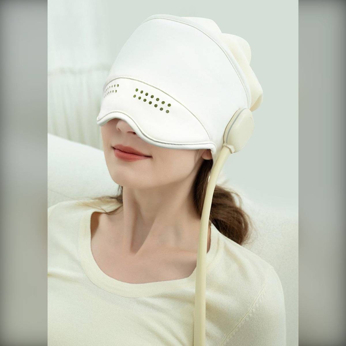 Frau, die ein weißes Augen- und Kopfmassagegerät trägt, gezeigt in einem Nahporträt vor hellem Hintergrund.