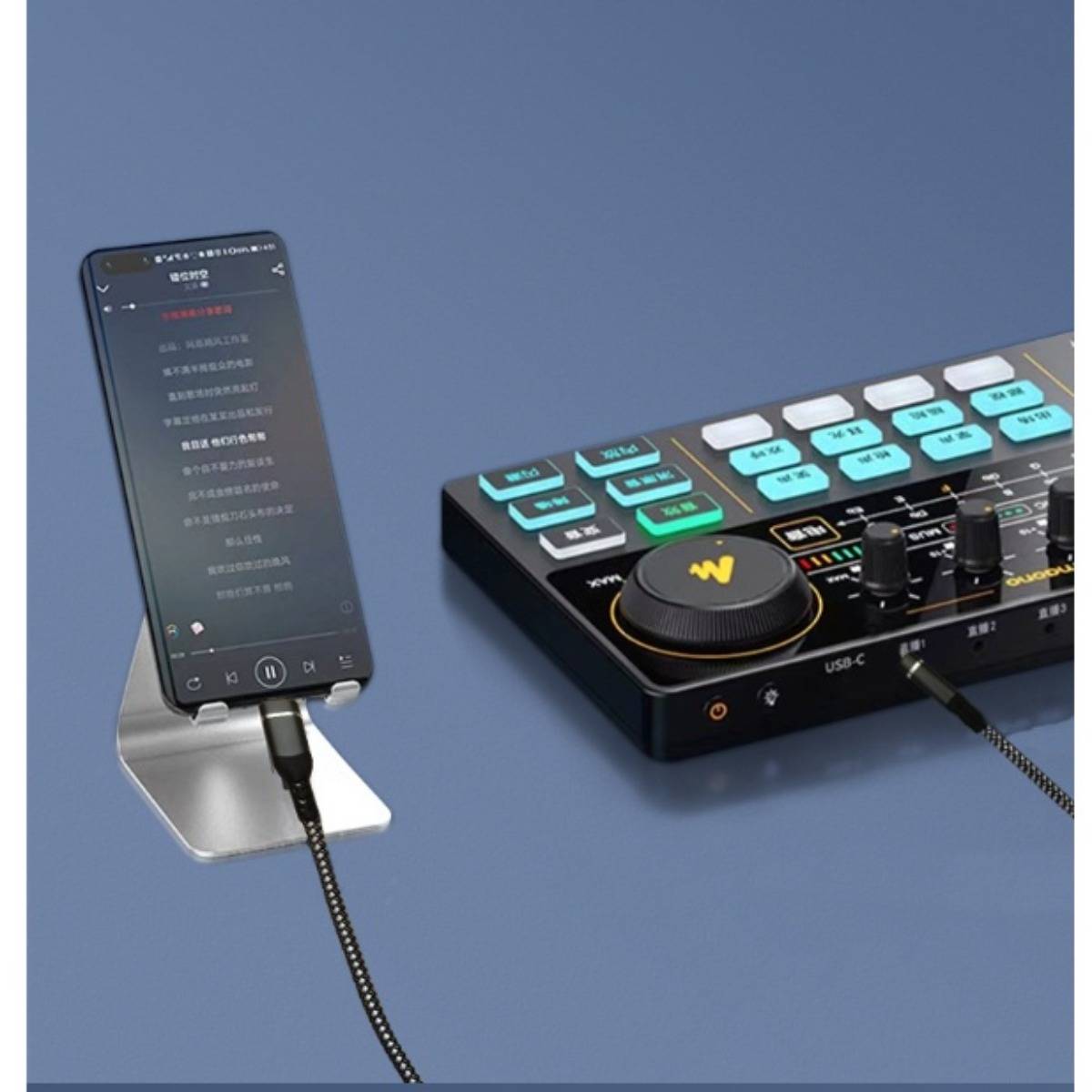 Ein Smartphone auf einem Ständer ist per Kabel mit einer kompakten Audio-Misch-/Steuerkonsole mit beleuchteten Tasten und Reglern verbunden.
