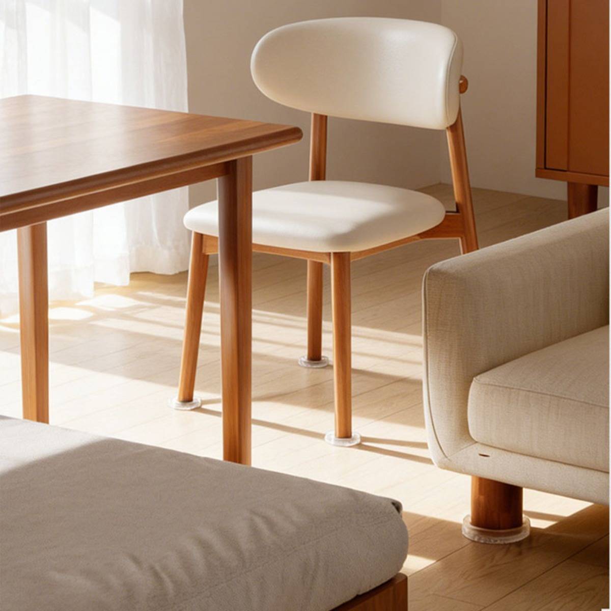 Ein sonnendurchfluteter moderner Raum mit einem weiß gepolsterten Stuhl neben einem Holztisch, einem beigen Sofa und einem niedrigen Hocker auf hellem Holzfußboden.