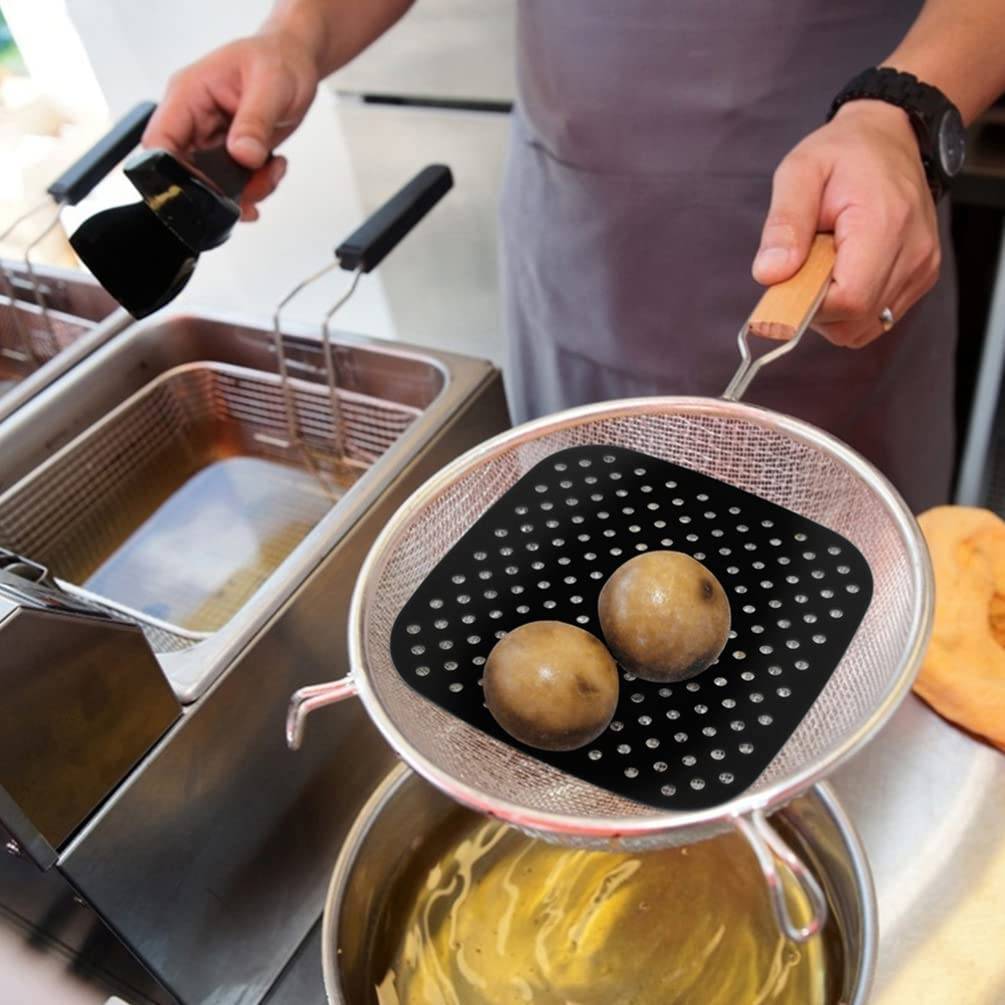 Kochen in einer Küchenfritteuse: zwei Kartoffelbälle ruhen in einem Abtropfkorb, während Öl in die Maschine gegossen wird.