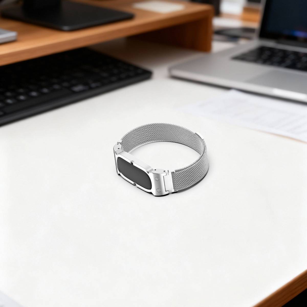 Ein silbernes Mesh-Uhrenarmband liegt auf einem weißen Schreibtisch, mit unscharfen Laptops im Hintergrund.
