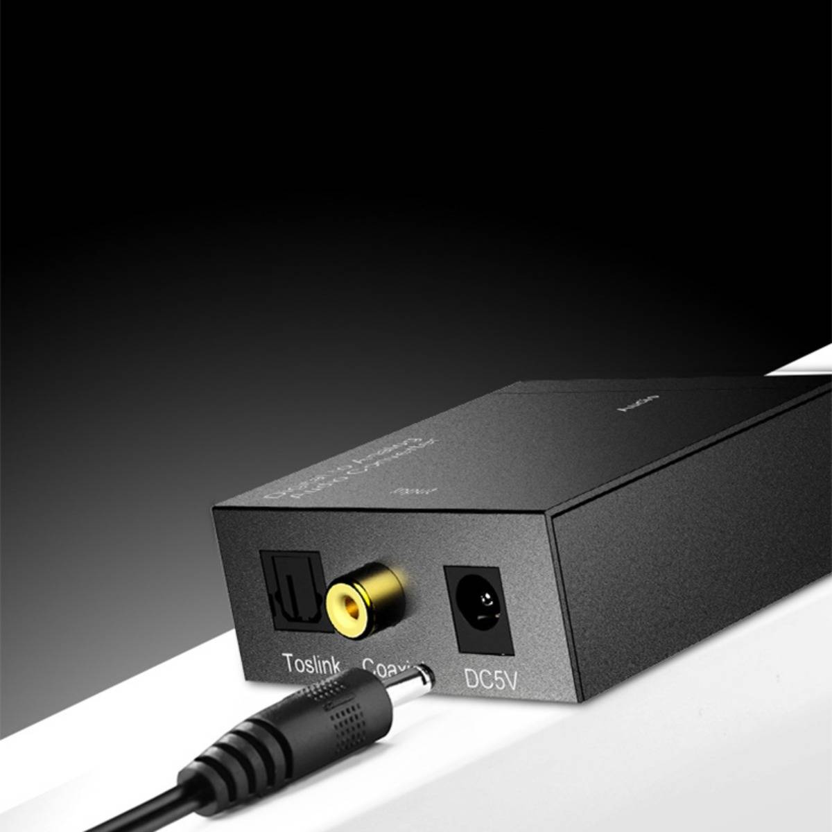 Nahaufnahme eines schwarzen Audiogerat-Rückpanels mit Toslink-Optik-, Koaxial- und DC 5V-Stromanschlüssen; ein Kabelstecker ist kurz davor, sich zu verbinden.