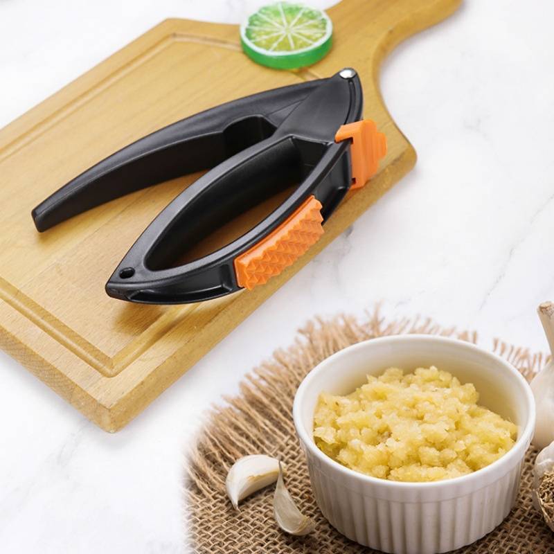 Schwarze tragbare Zitrusfruchtpresse auf einem Schneidebrett mit einer halbierten Limette, Knoblauchzehen und einer Schüssel mit gehacktem Knoblauch auf einer Jutumunterlage.