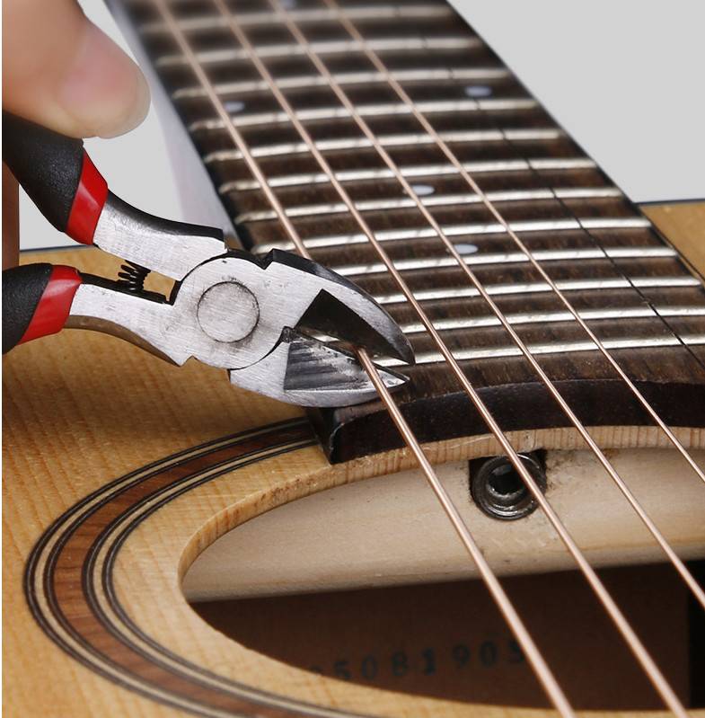 Nahaufnahme einer Zange, die eine Gitarrensaite in der Nähe des Stegs abschneidet, was auf einen Saitenwechsel oder eine Reparatur hindeutet.