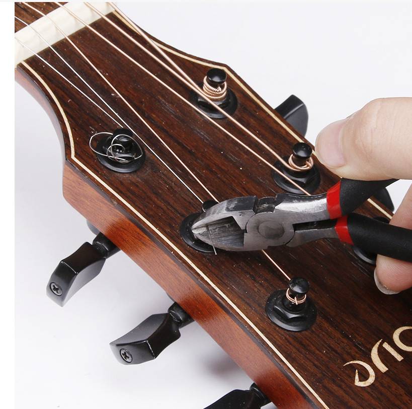 Nahaufnahme einer Hand, die mit einer Drahtschere Saiten am Gitarrenkopf während des Stimmens oder Umspannens schneidet.