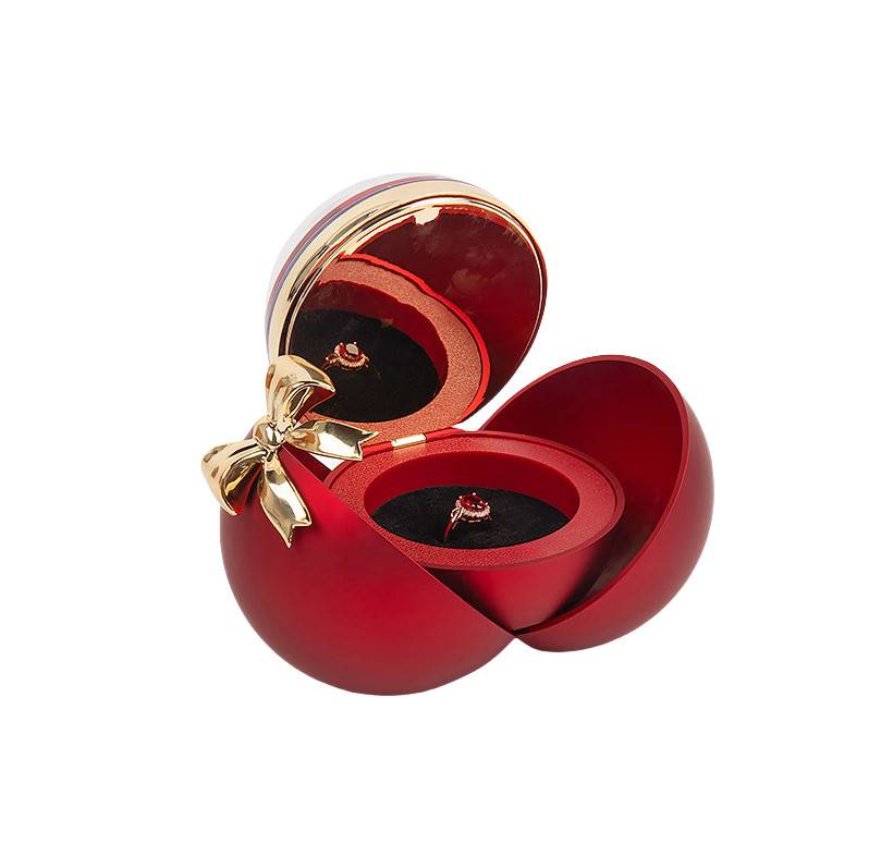 Rote herzförmige Schmuckschatulle, offen mit einem Ring im Inneren, mit einer goldenen Schleife auf der Vorderseite.