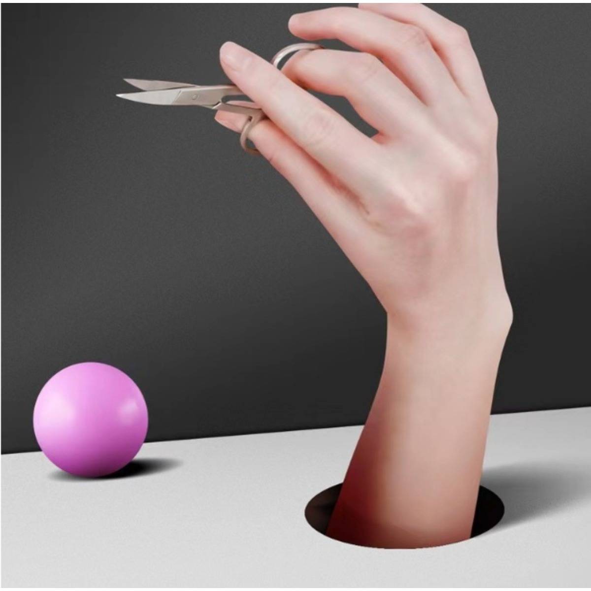 Eine Hand taucht aus einem Loch in einer Oberfläche auf und hält eine Schere in der Nähe eines rosa Balls vor einem dunklen Hintergrund.