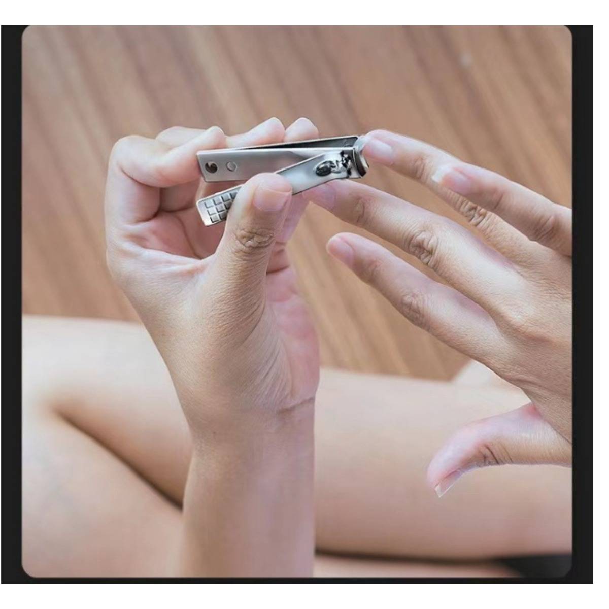 Nahaufnahme von Händen, die eine Nagelschere verwenden, um Fingernägel auf einer Holzoberfläche zu schneiden.