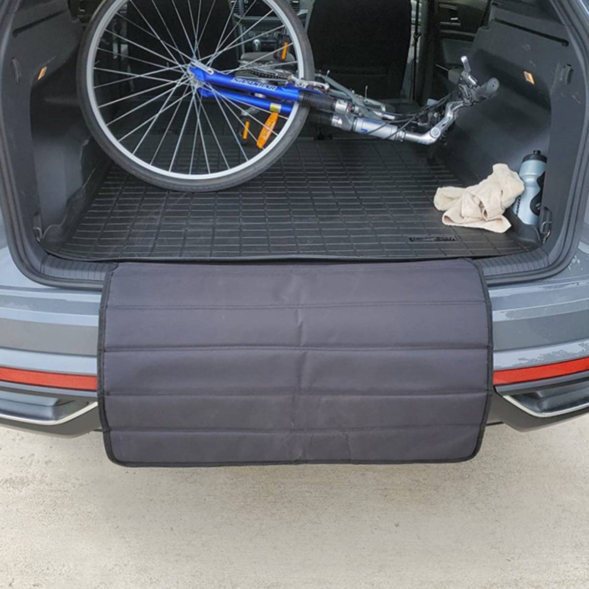Fahrrad im Kofferraum eines SUV geladen, mit offener Heckklappe und einem gepolsterten schwarzen Ladeschutz, der über die Stoßstange hängt.