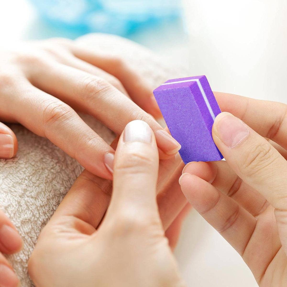 Maniküre-Hände mit einer Feile an einem natürlichen Fingernagel mit einem lila Nagelpuffer während einer Maniküre.
