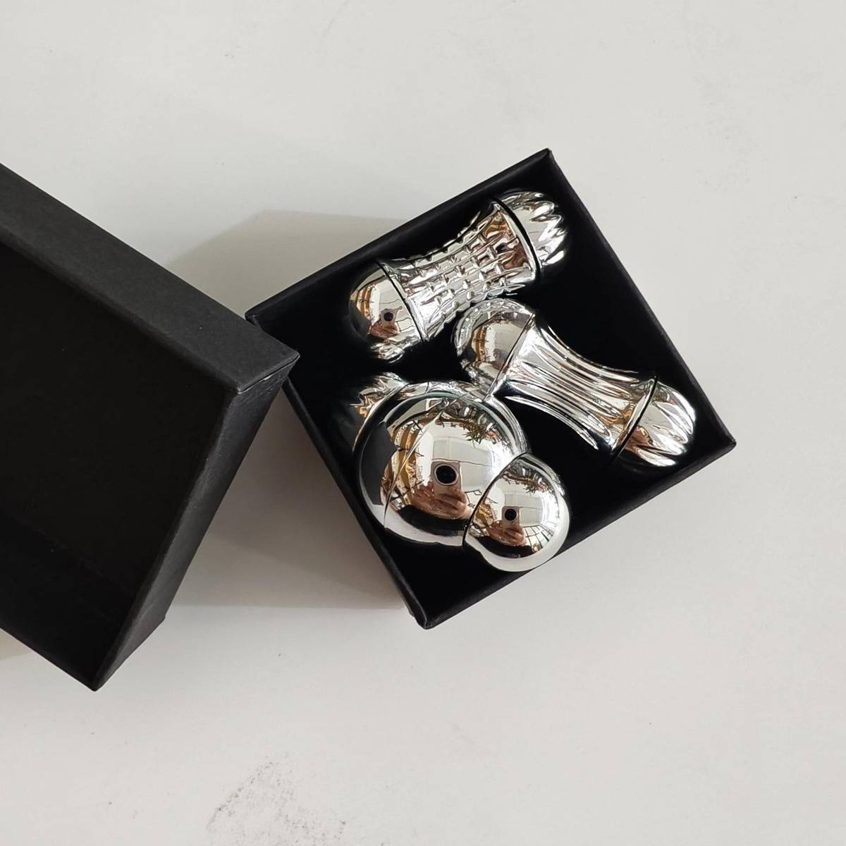 Offene schwarze Geschenkbox mit vier glänzenden silbernen dekorativen Ornamenten auf einer weißen Oberfläche.
