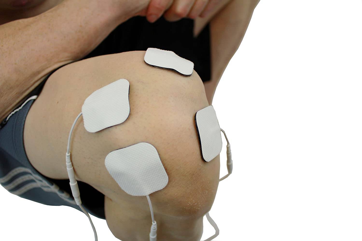 Nahaufnahme eines gebeugten Knies einer Person mit vier klebenden Elektrodenpflastern, die auf der Haut angebracht sind und auf elektrische Muskelstimulation oder Physiotherapie hindeuten.