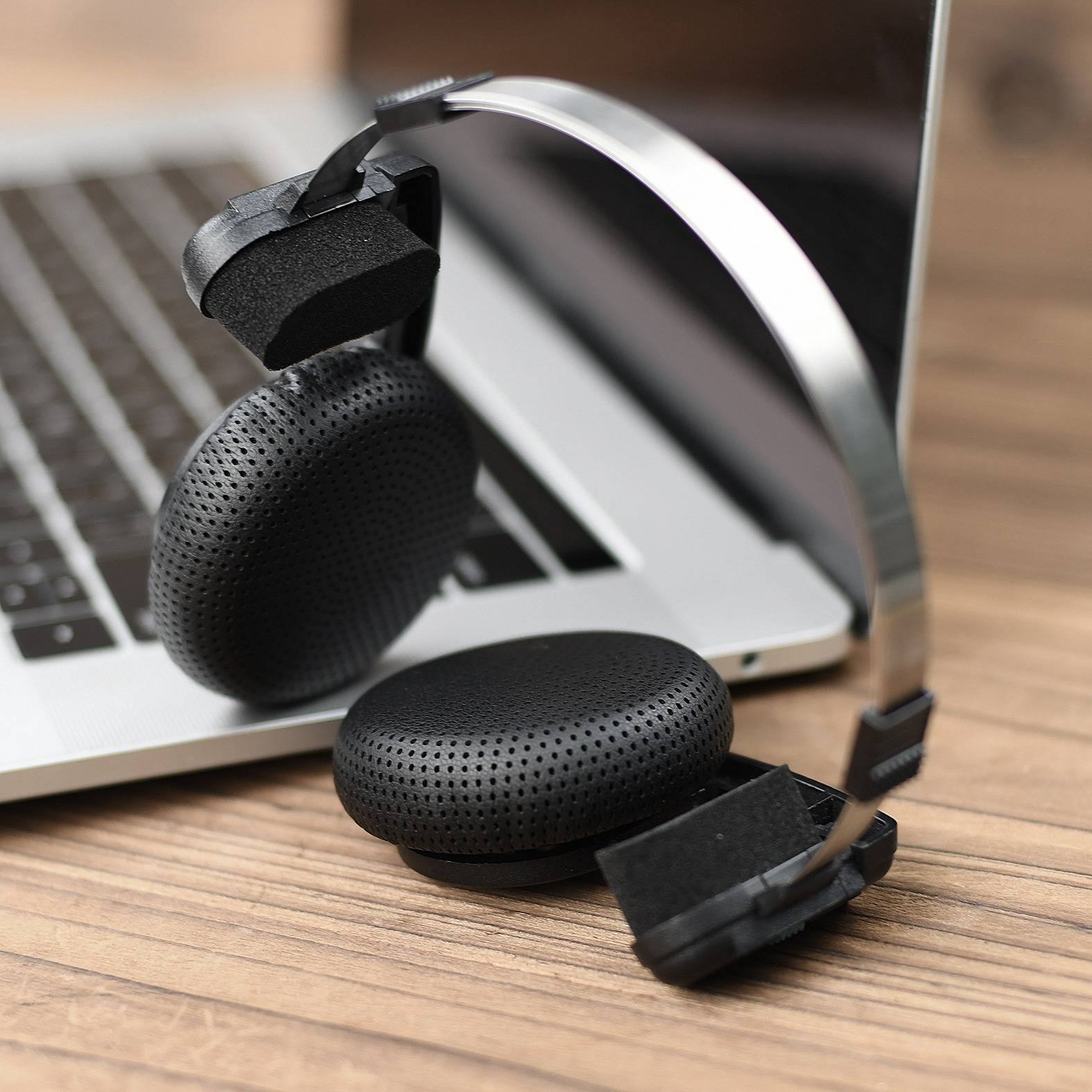 Schwarze Over-Ear-Kopfhörer, die auf einer Laptop-Tastatur auf einem Holzschreibtisch ruhen