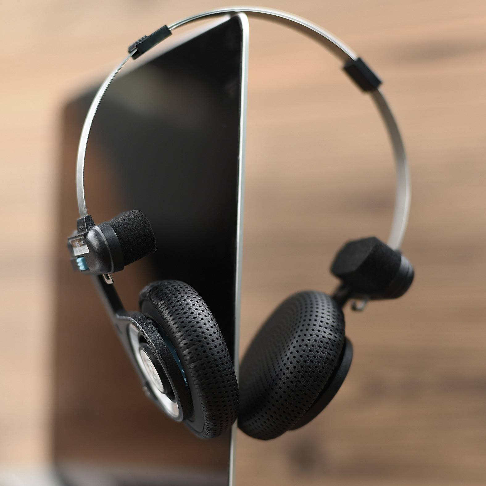 Schwarzes Smartphone mit um die Ohren gelegten Over-Ear-Kopfhörern auf einer Holzoberfläche.