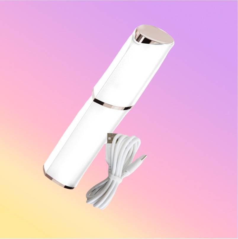 Weißes zylindrisches tragbares Gerät mit goldenen Akzenten und einem USB-Ladekabel auf einem rosafarbenen bis gelben Farbverlauf-Hintergrund.