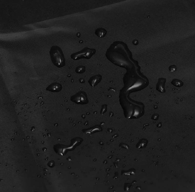 Nahaufnahme einer schwarzen Oberfläche mit verstreuten Wassertropfen, einige größere Perlen reflektieren das Licht.