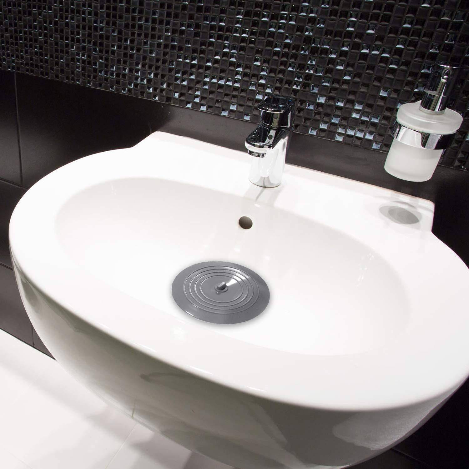 Ovales weißes Badezimmerbecken mit verchromtem Wasserhahn und Seifenspender vor einer dunklen Mosaikfliesenwand.