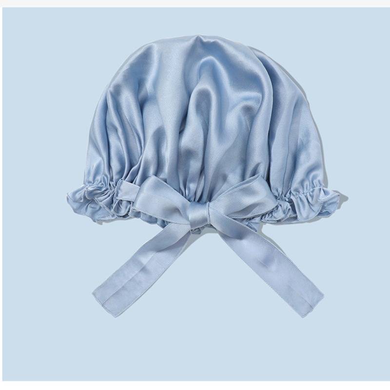 Hellblaue Satinhaube mit gerüschter elastischer Kante und gebundenem Schleifenbogen auf hellblauem Hintergrund.