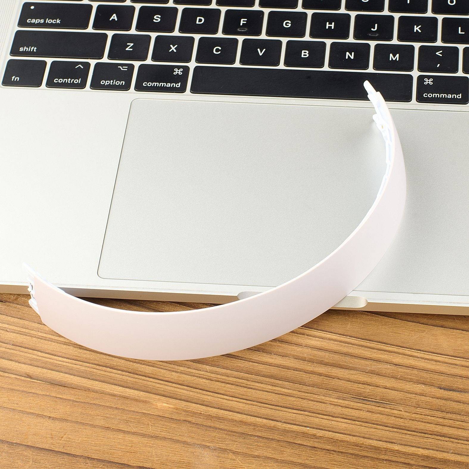 Ein weißer Papierstreifen oder ein weißes Armband liegt über einem Laptop-Trackpad und einer Tastatur auf einem Holzschreibtisch.