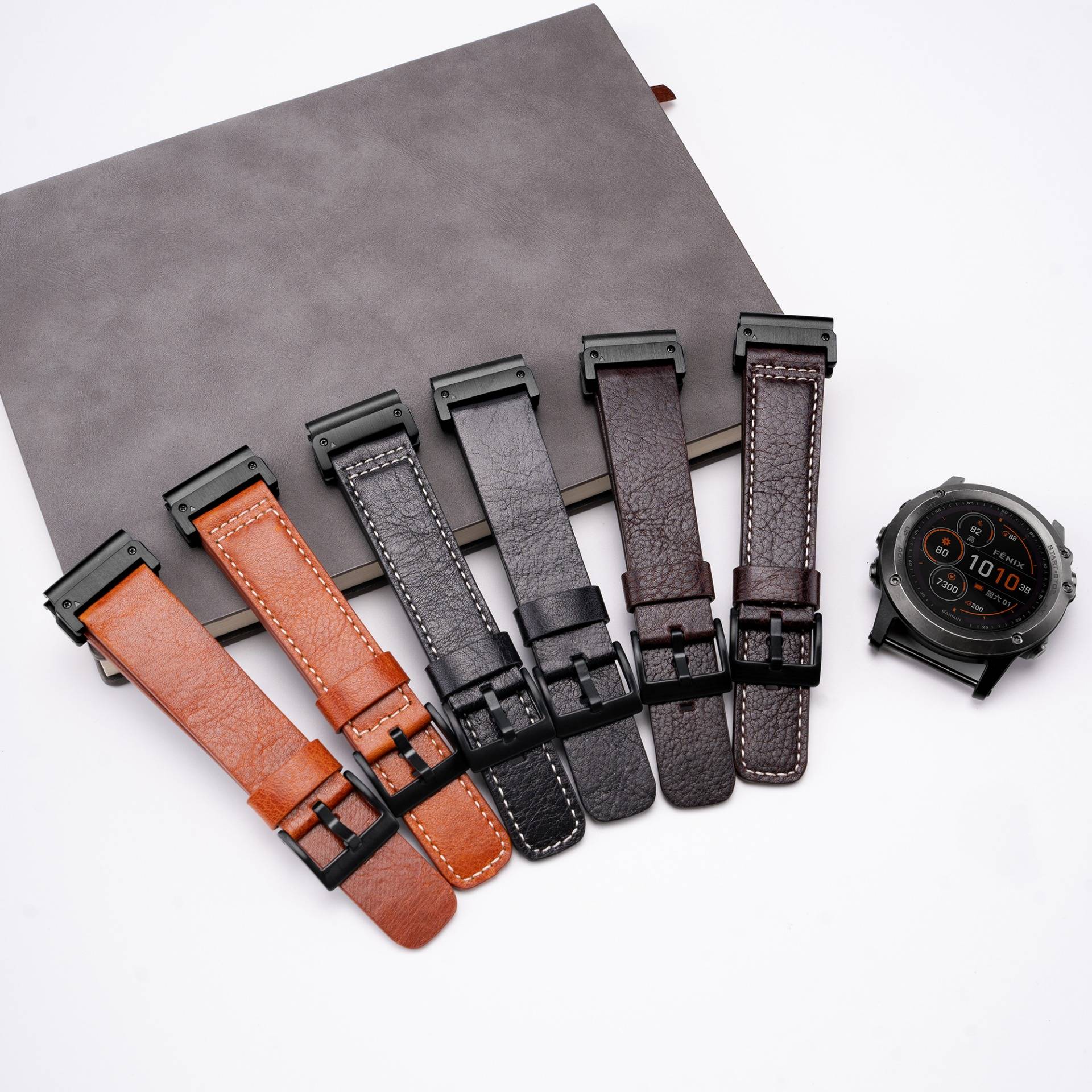 Sechs austauschbare Smartwatch-Armbänder in Braun, Orange, Grau und Schwarz, neben einer Smartwatch angeordnet, zeigen verschiedene Bandoptionen.