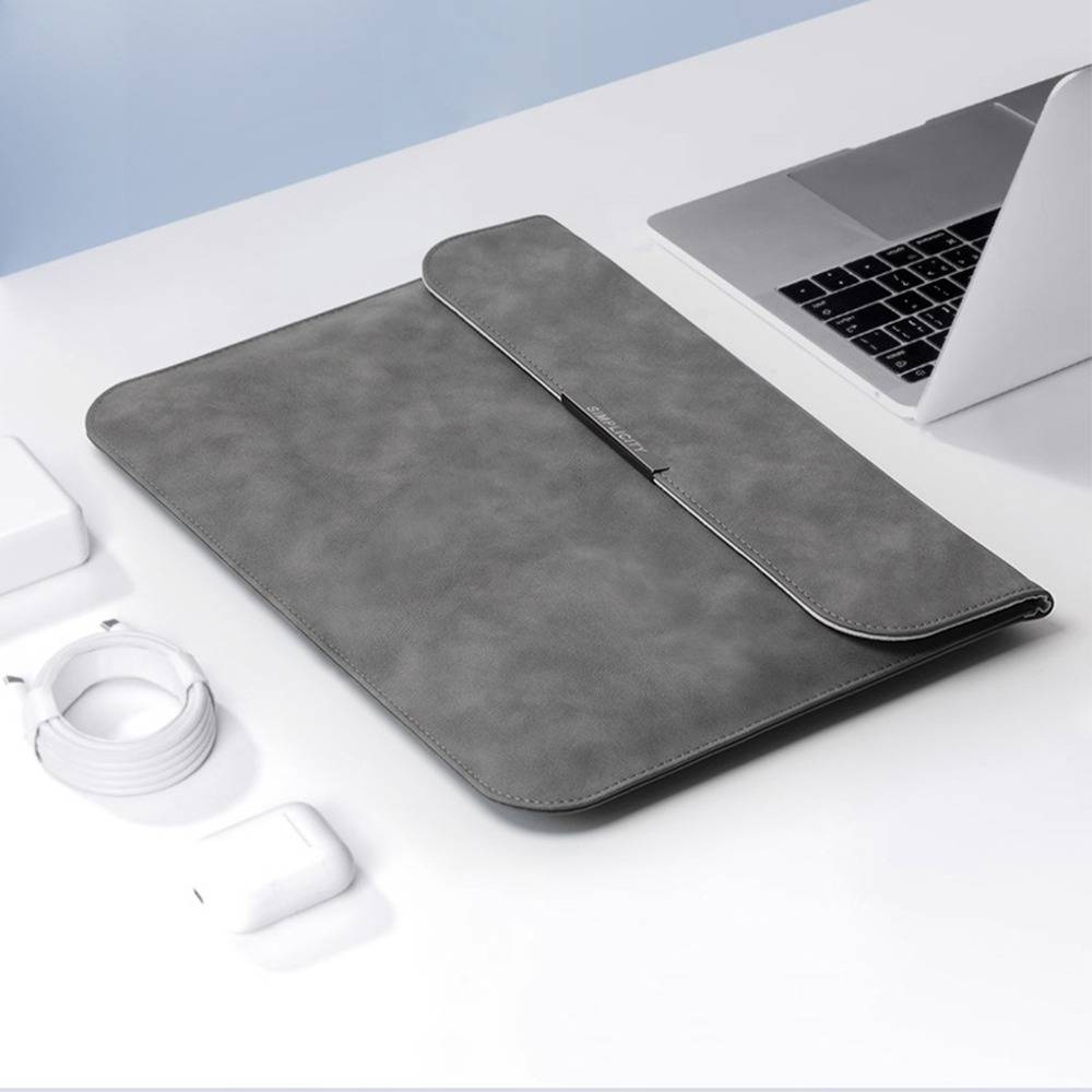 Graue Laptop-Schutzhülle mit Reißverschluss auf einem weißen Schreibtisch neben einem aufgeklappten Laptop, mit Ladekabel und Kopfhörern in der Nähe.