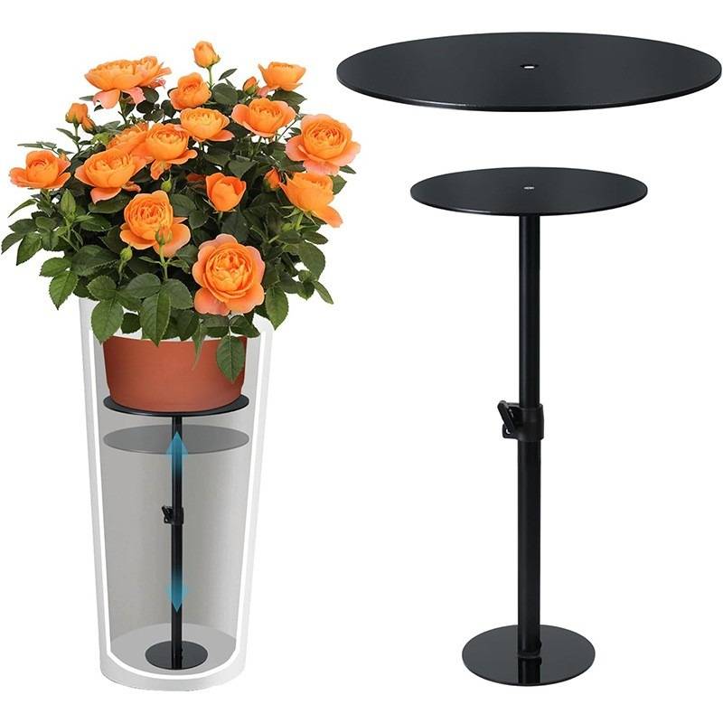 Diagramm, das einen ausziehbaren Pflanzenständer mit einem Topf orangefarbener Blumen auf einer unteren Plattform und einer erweiterten schwarzen Tischplatte oben zeigt, was die einstellbare Höhe angibt.