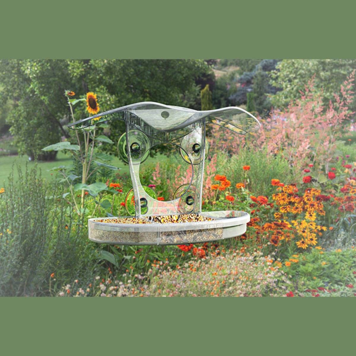 Dekorativer Vogelfutterhaus oder Gartenskulptur, das über einem blütenreichen Gartenbeet schwebt, mit geschwungenem Metall- und Glasrahmen und Futtertablett.