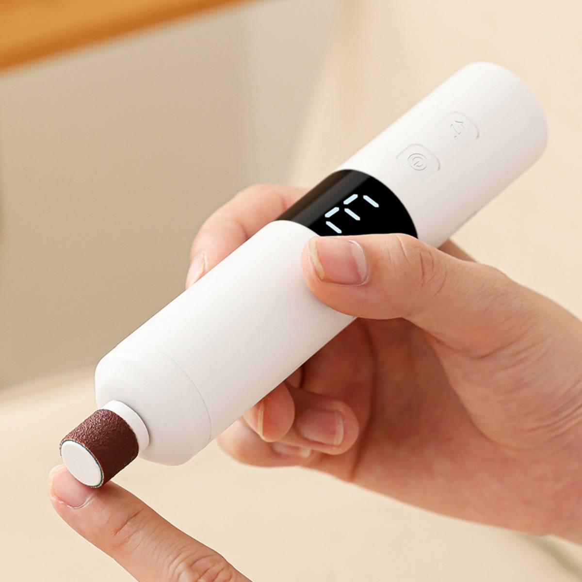 Tragbare elektrische Nagelfeile, die einen Fingernagel bearbeitet, mit einer rotierenden Schleifspitze und kleinem digitalen Display.