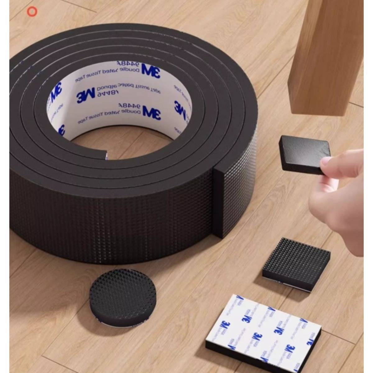 Rolle schwarzes Klebeband aus Schaumstoff mit separaten quadratischen und runden Pads auf einem Holzboden, wobei ein Pad von einer Hand gehalten wird.