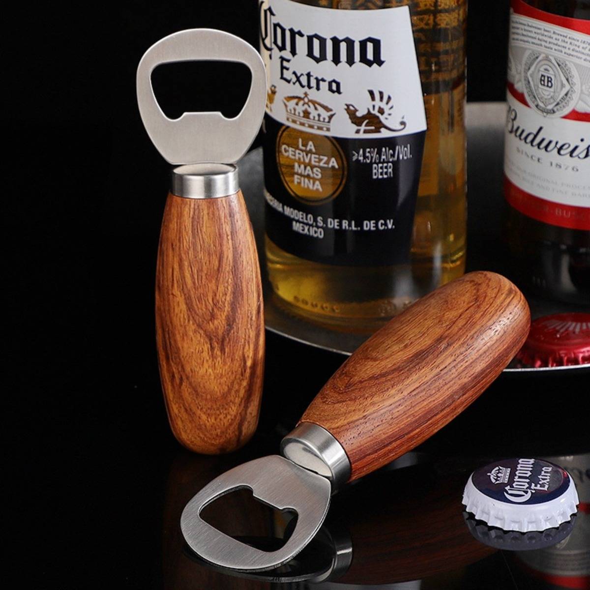 Zwei Flaschenöffner mit Holzgriffen auf einer dunklen Oberfläche mit Bierflaschen und einer Corona-Kappe im Hintergrund.