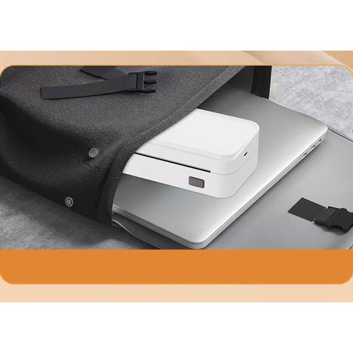 Offener schwarzer Stoff-Ärmel, der einen silbernen Laptop schützt, mit einem weißen kompakten Gerät darin; ein Riemen liegt daneben auf einem Tisch.