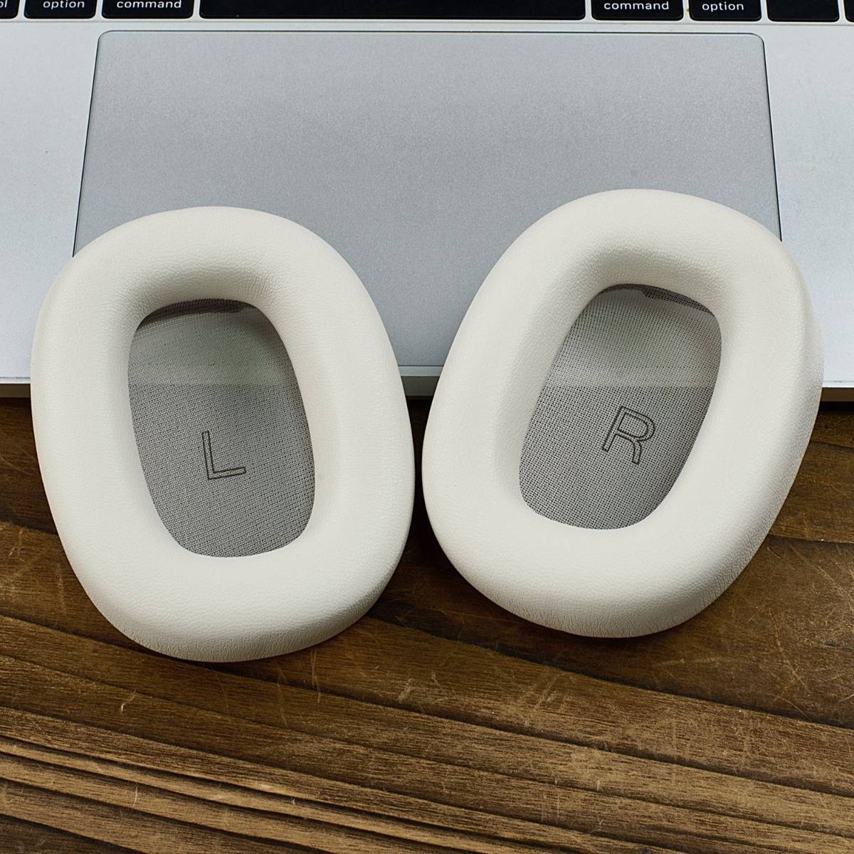 Weiße Over-Ear-Kopfhörerohrmuscheln mit den Bezeichnungen „L" und „R"", die vor einem Laptop-Trackpad liegen.