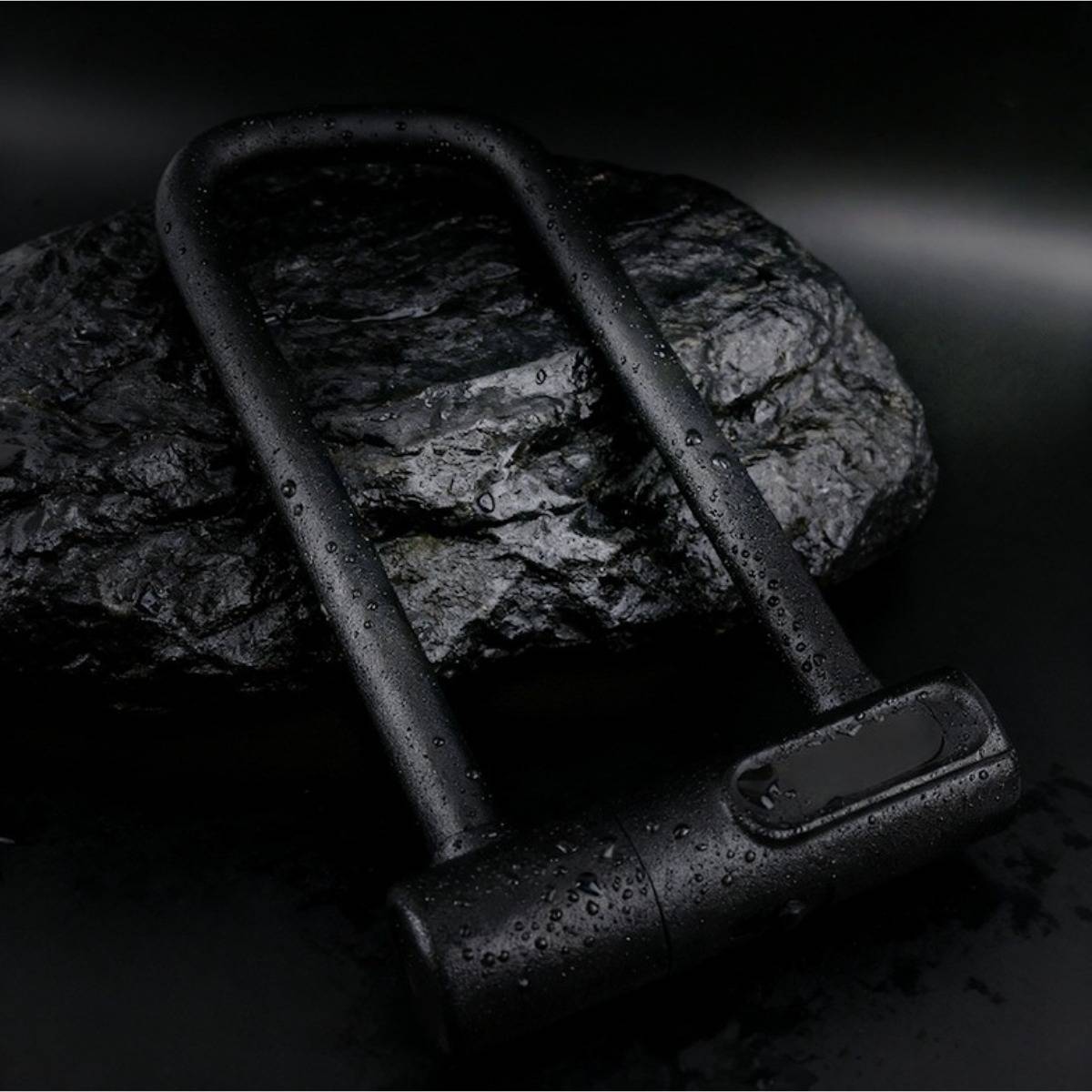 Schwarzes Metallvorhängeschloss, das quer über einen rauen Stein auf dunklem Hintergrund liegt, dargestellt mit Wassertropfen.