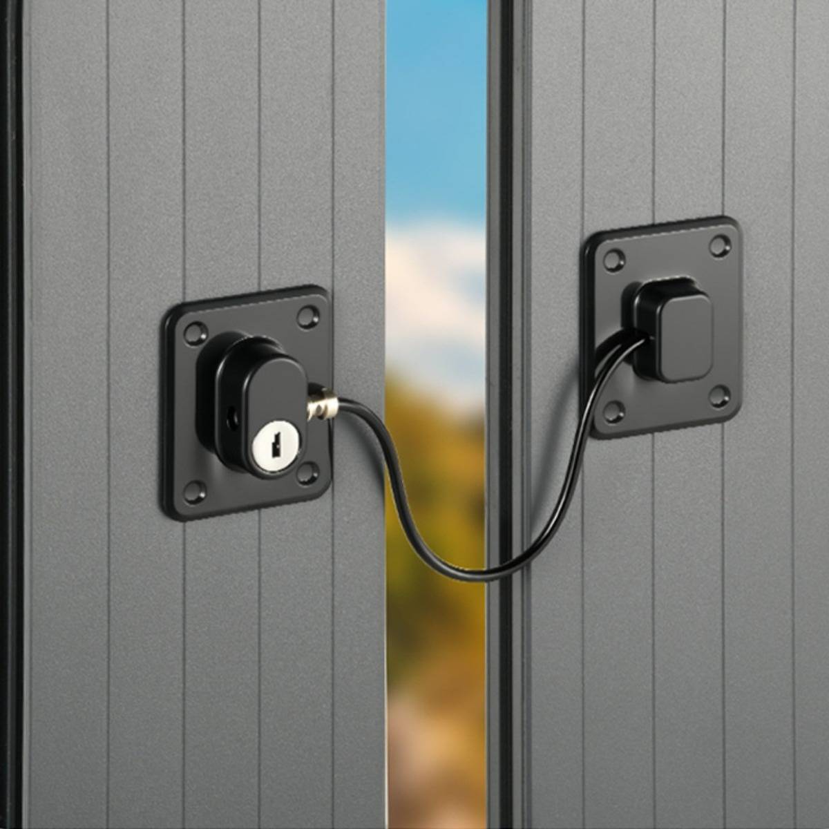 Ein schwarzes Türschloss, das mit einem Kabel an einem zweiten montierten Schloss auf einem anderen Panel befestigt ist und zwei graue Türen zusammenhält.