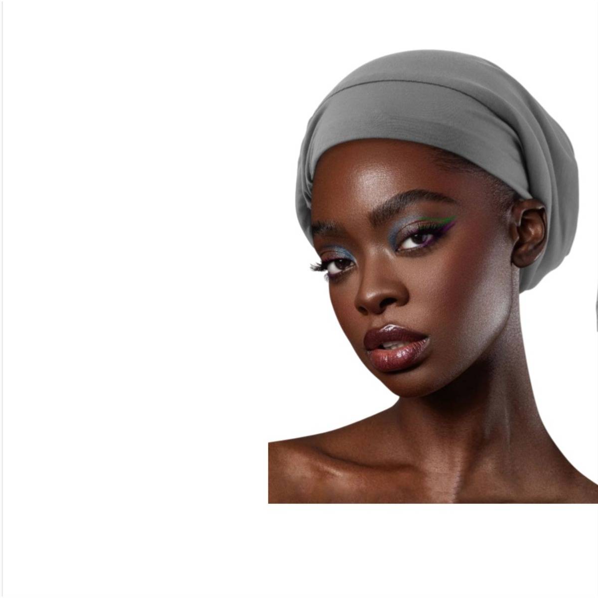 Porträt einer Frau mit dunkler Hautfarbe, die ein graues Kopftuch trägt und Make-up trägt, vor einem weißen Hintergrund posiert.