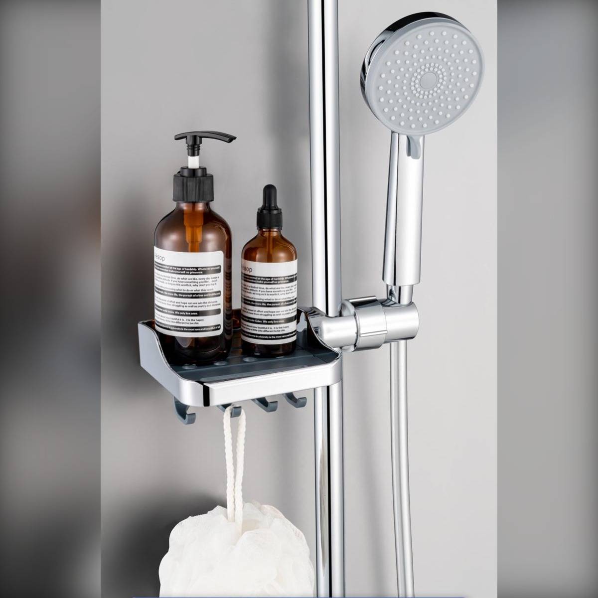 Duschablage mit zwei bernsteinfarbenen Pumpflaschen und einer Tropferflasche neben einem Handbrausekopf, mit einem hängenden Luffa darunter.