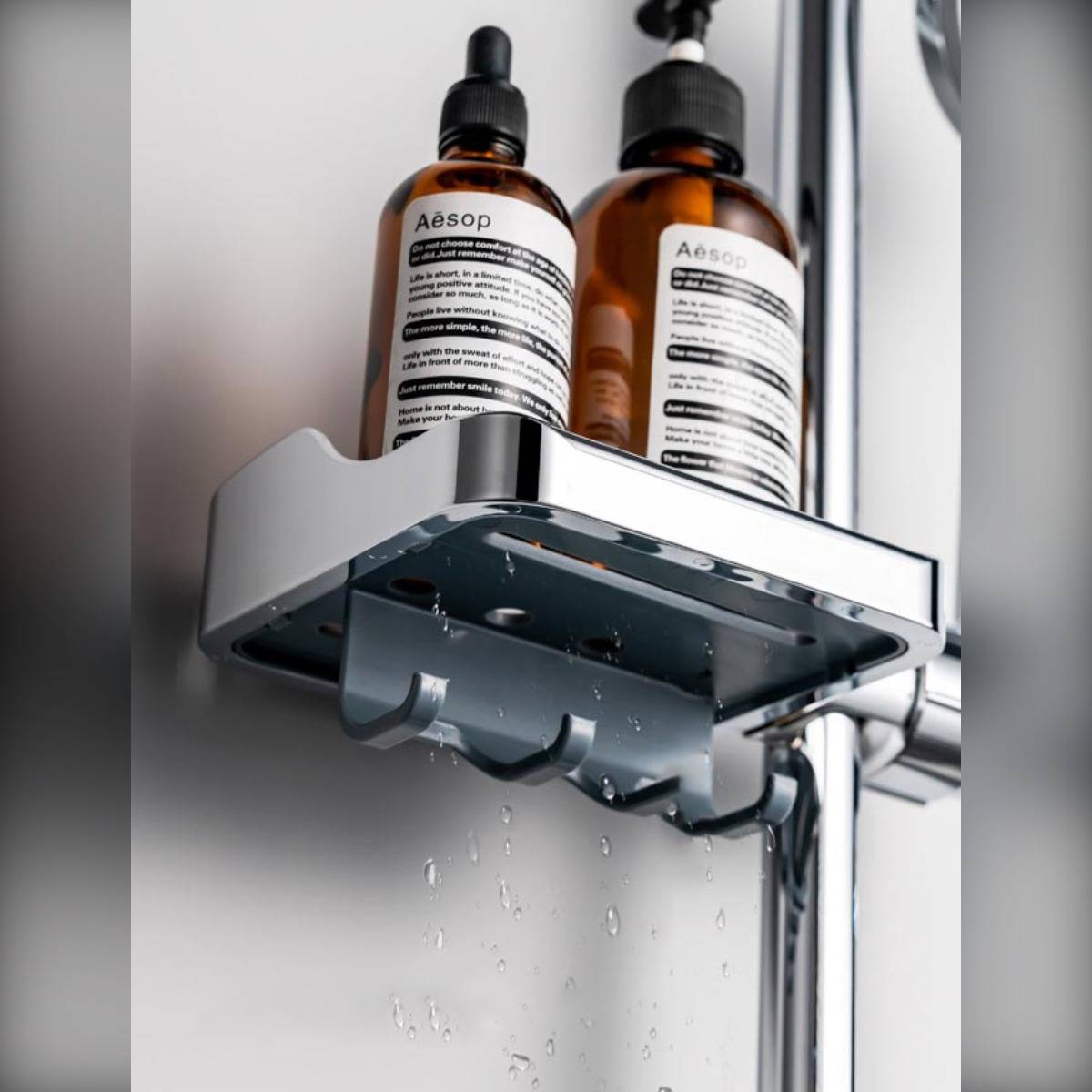 Chromablage mit Duschkopf hält zwei Aesop-Flaschen, Wasser tropft von der Unterseite herab