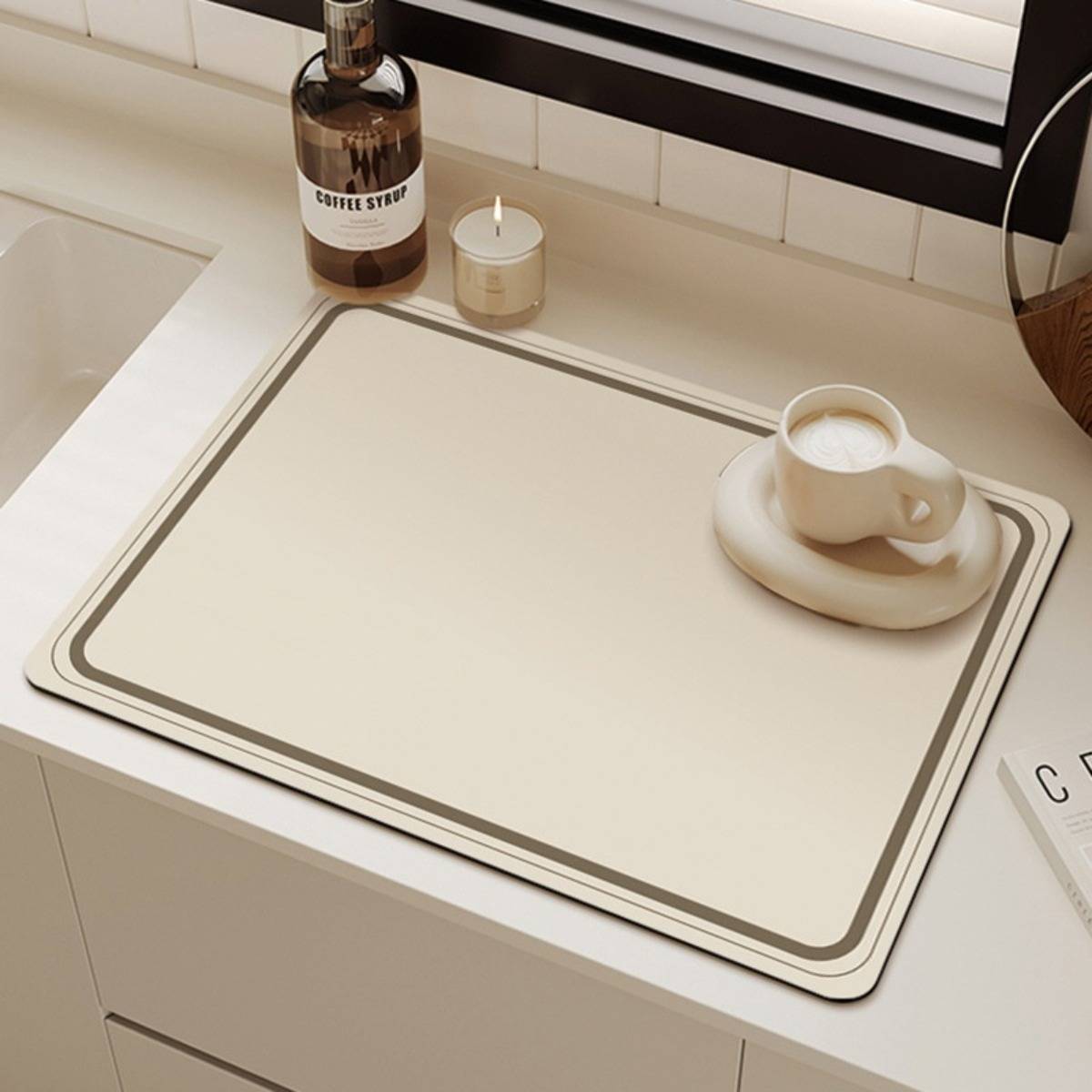 Minimale Küchentheke mit einem cremefarbenen Tablett, einer Kaffeetasse auf einer Untertasse, einer Kaffeesirupflasche und einer kleinen Kerze neben dem Fenster.