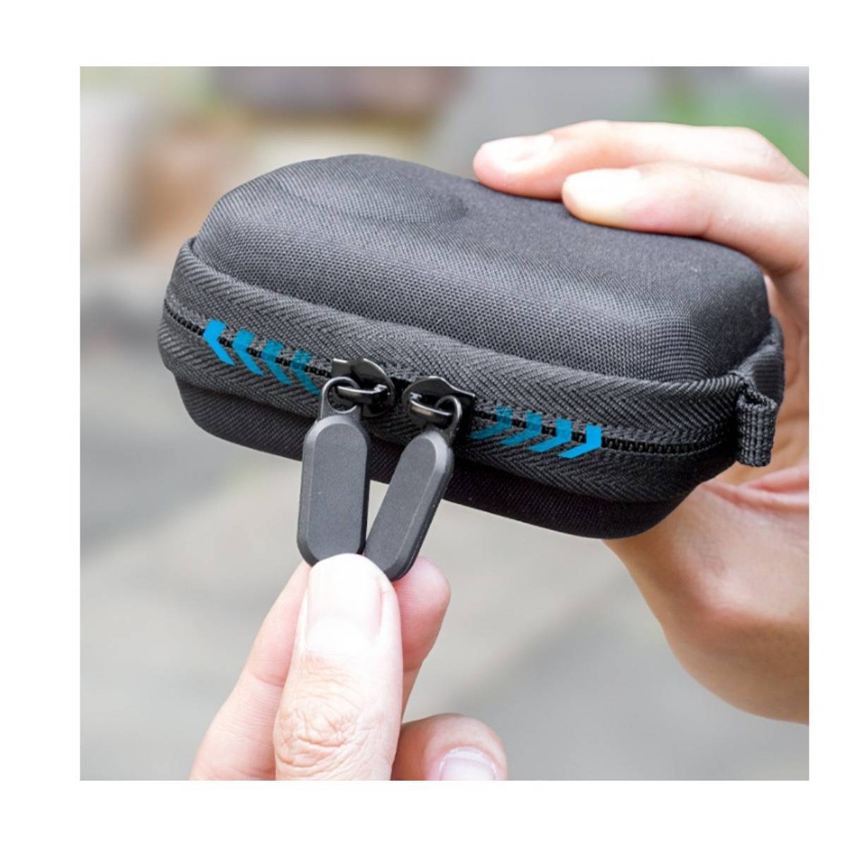 Hände, die ein kleines schwarzes Etui mit Reißverschluss und blauen Akzenten öffnen, wobei die Reißverschluss-Schieber und Zuglasche aus nächster Nähe zu sehen sind.