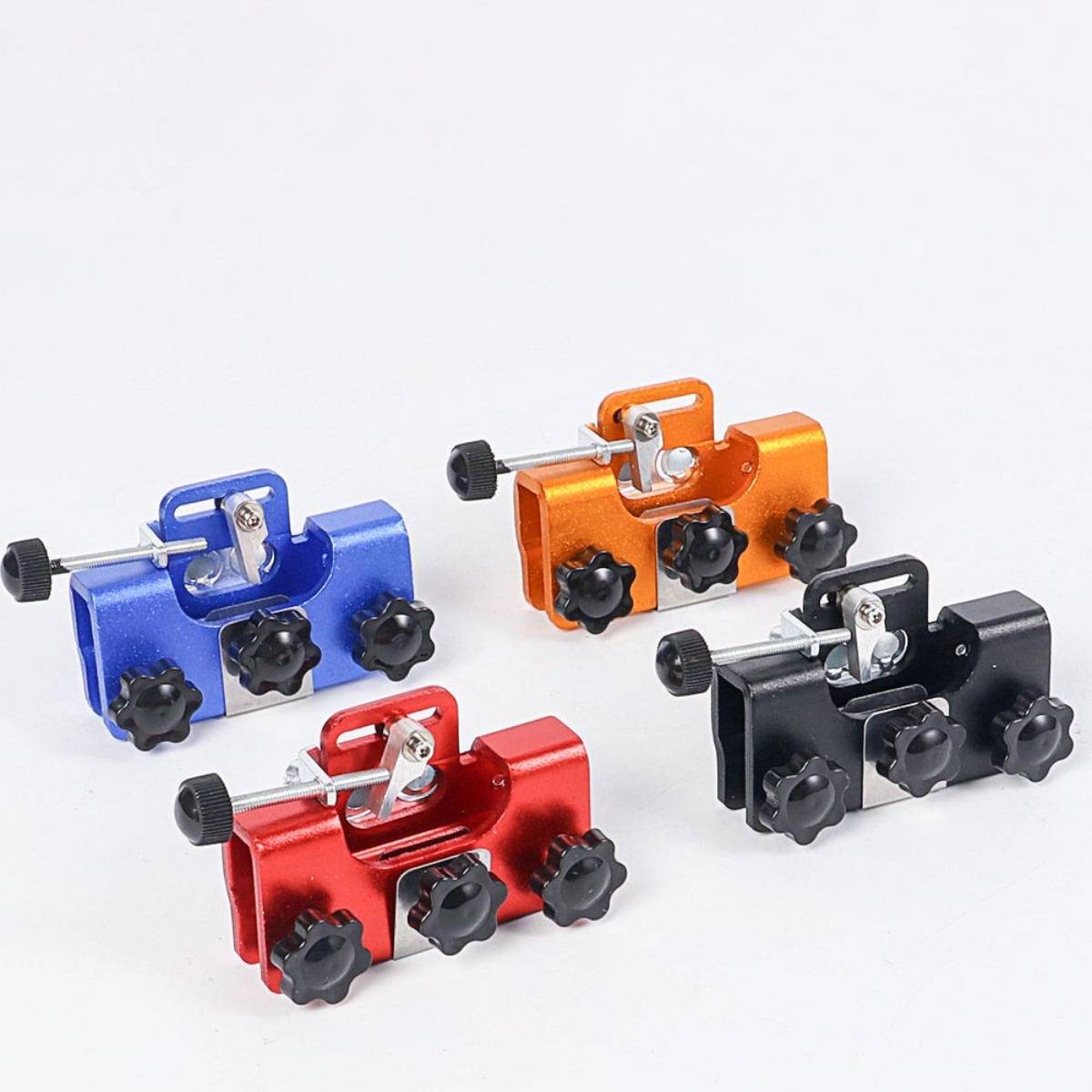 Vier farbenfrohe Metallklammern oder -halter in Blau, Orange, Rot und Schwarz, angeordnet auf weißem Hintergrund.
