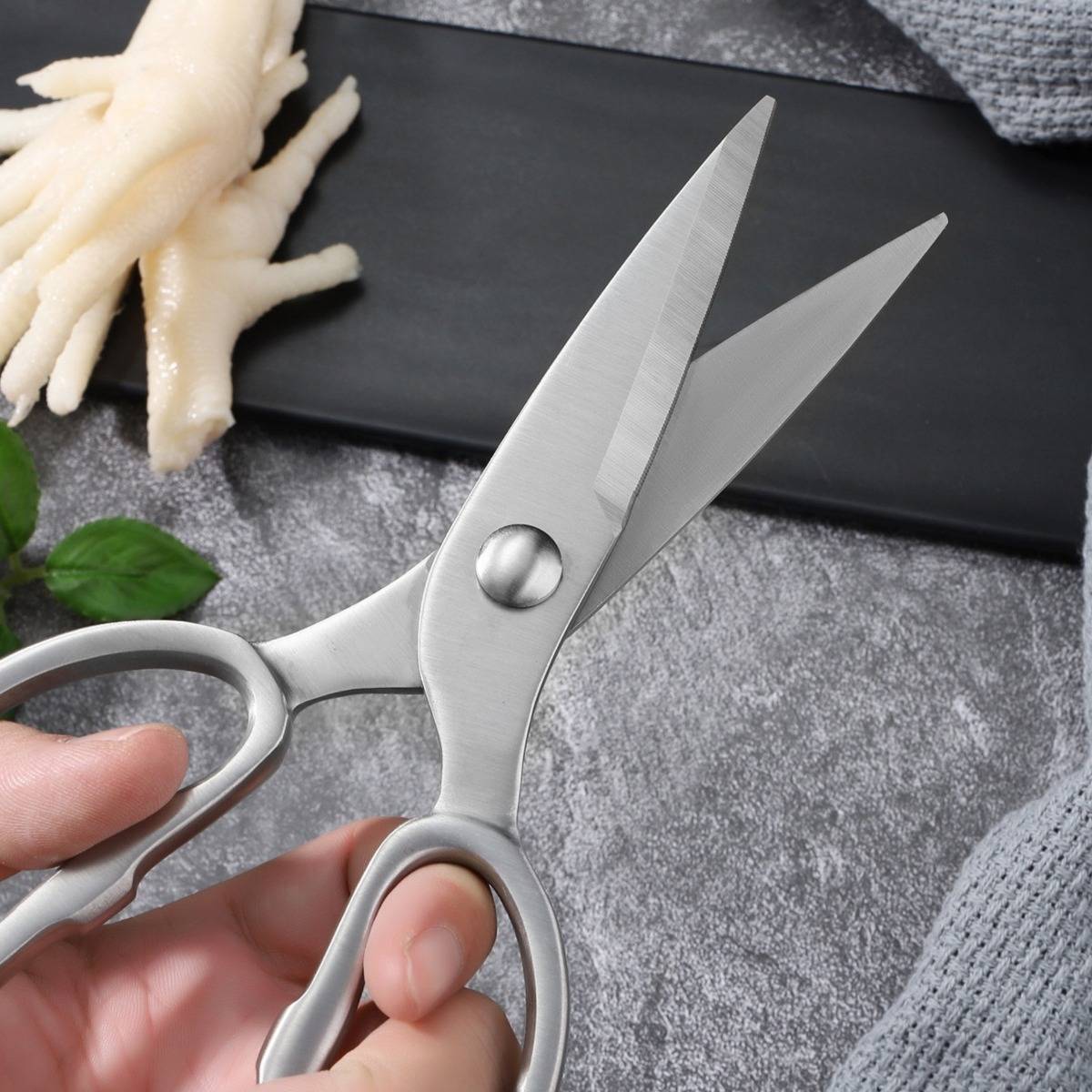Nahaufnahme einer Hand, die silberne Schere neben Hühnerfüßen auf einem Schneidebrett hält, was auf Essensverarbeitung oder Schlachtung hindeutet.