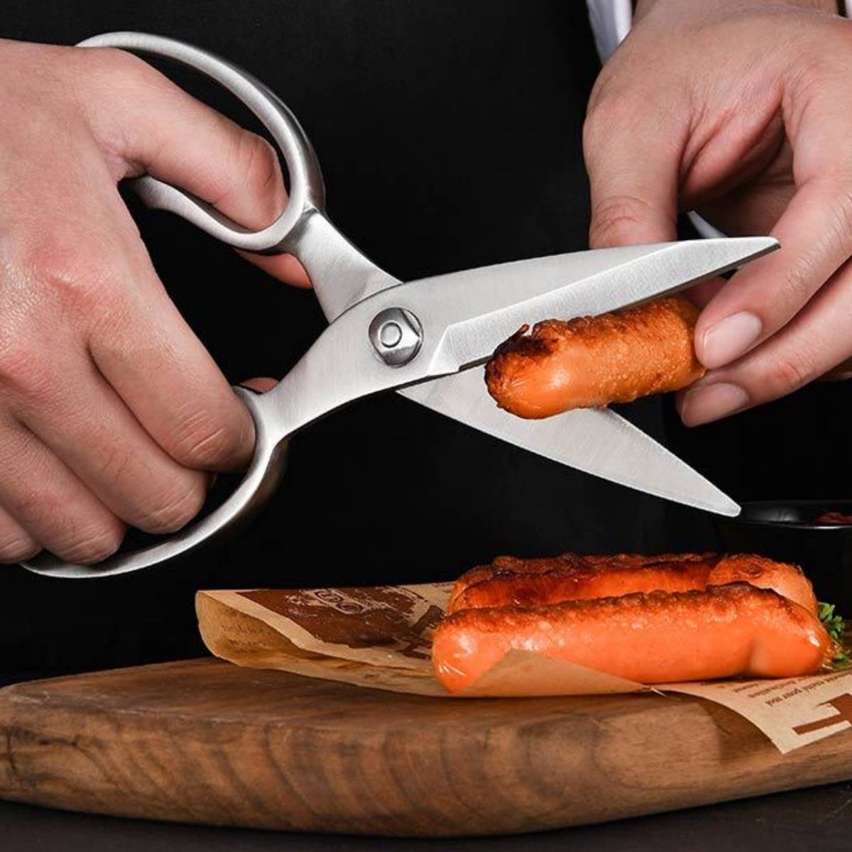 Hände, die eine Schere benutzen, um ein Hot Dog über einem Servierbrett zu schneiden, mit einem weiteren Hot Dog darunter.