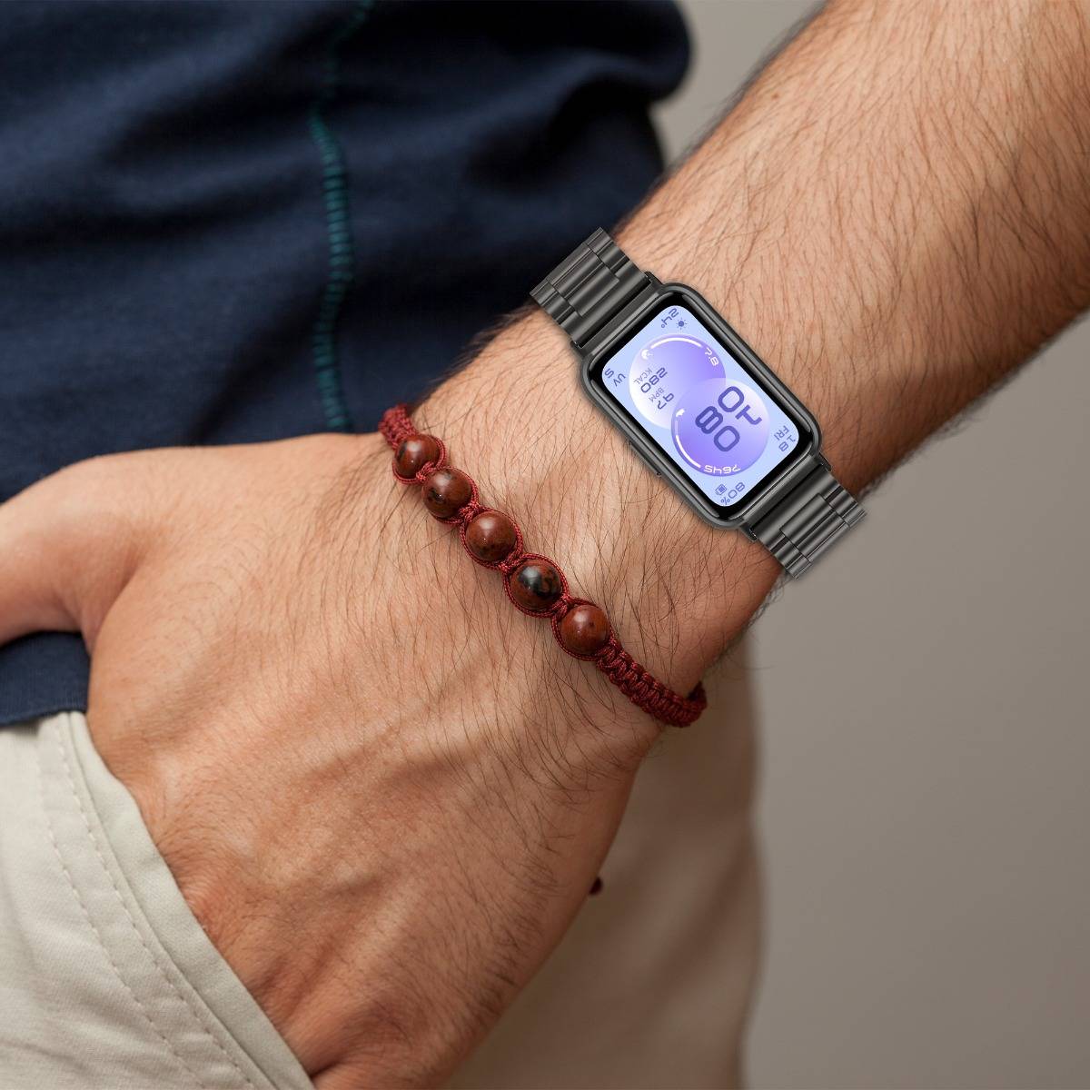 Nahaufnahme eines Handgelenks, das eine Smartwatch mit lila digitalem Display und ein rotes Perlenarmband trägt.