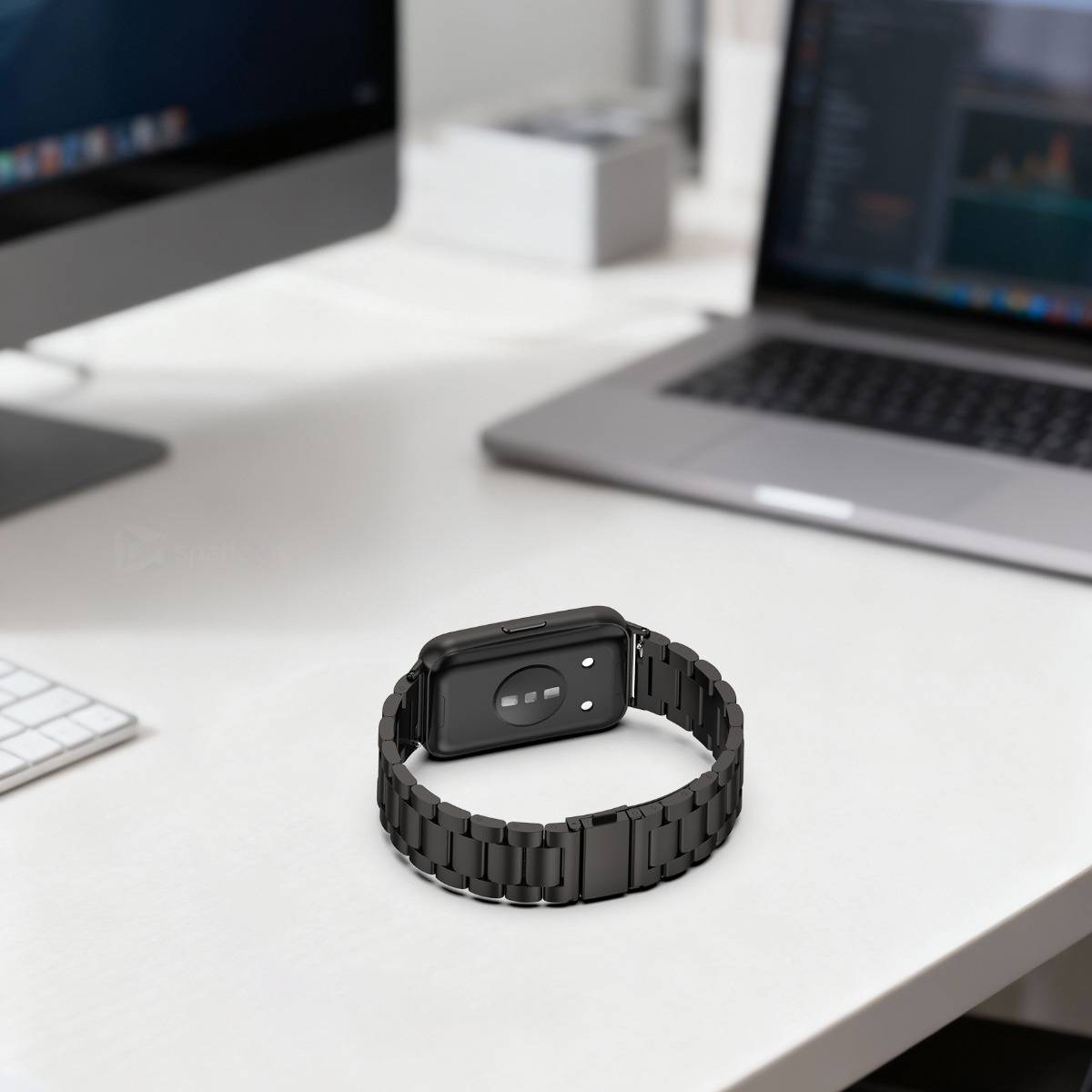 Schwarze Smartwatch mit Armband auf einem weißen Schreibtisch zwischen zwei aufgeklappten Laptops in einem modernen Arbeitsbereich.