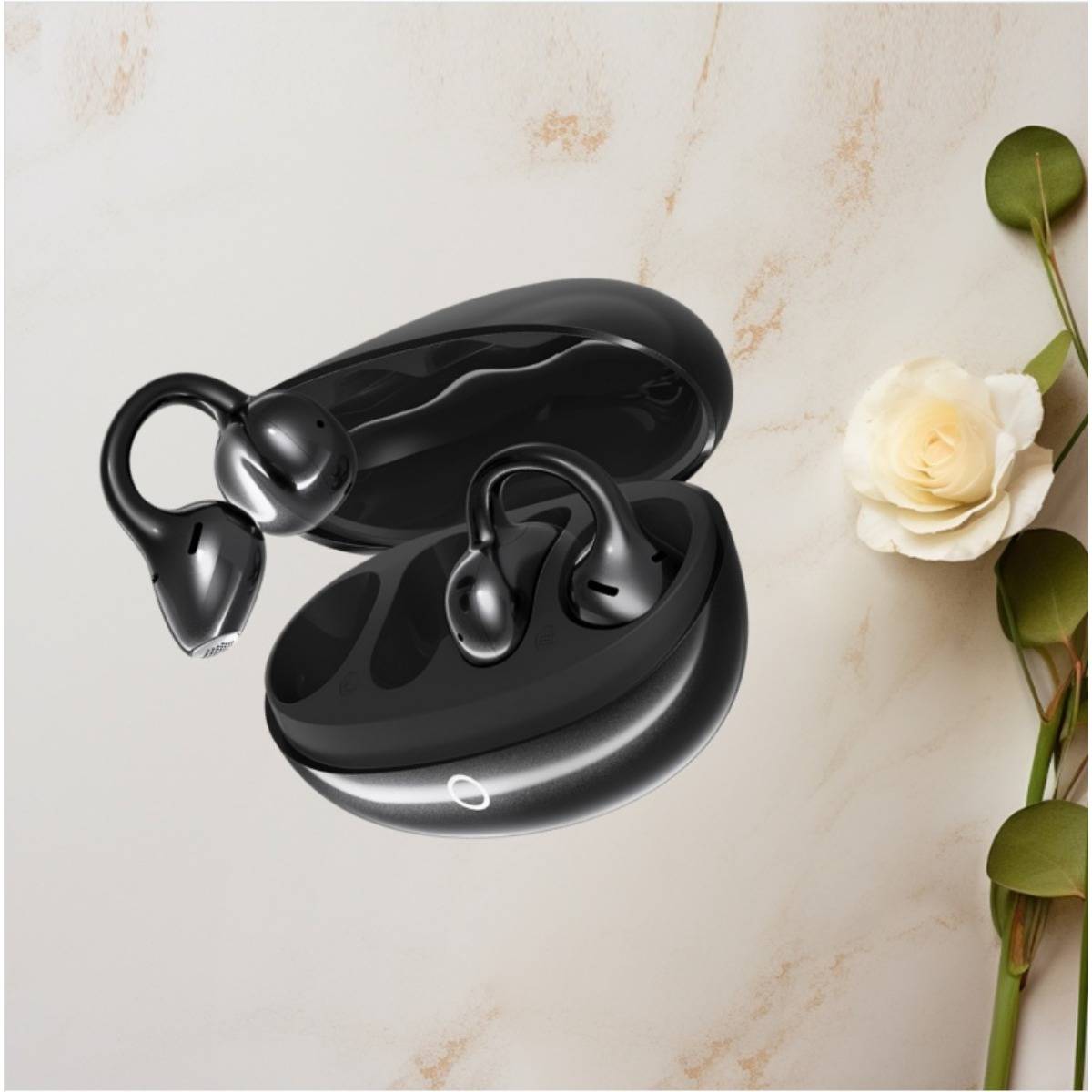 Schwarze kabellose Ohrhörer in einem offenen Ladeetui auf einer hellen Marmorflache, mit einer weißen Rose und grünem Stiel daneben.