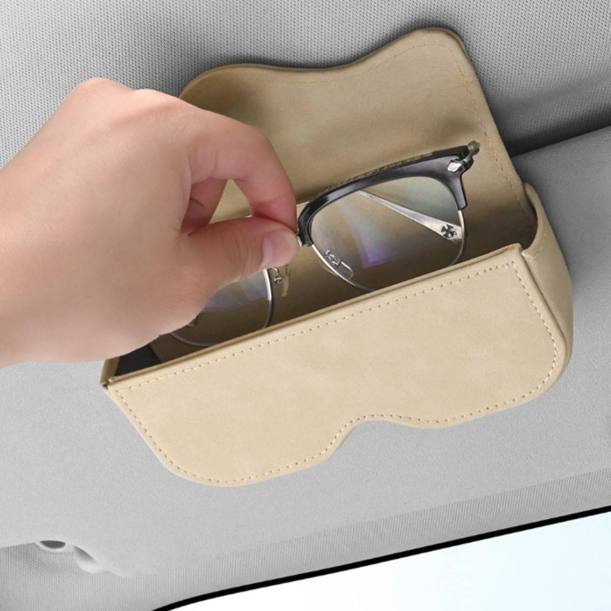 Hand, die eine Brille in einen beigen Sonnenbrillenhalter legt, der an einer Sonnenblende eines Autos befestigt ist.