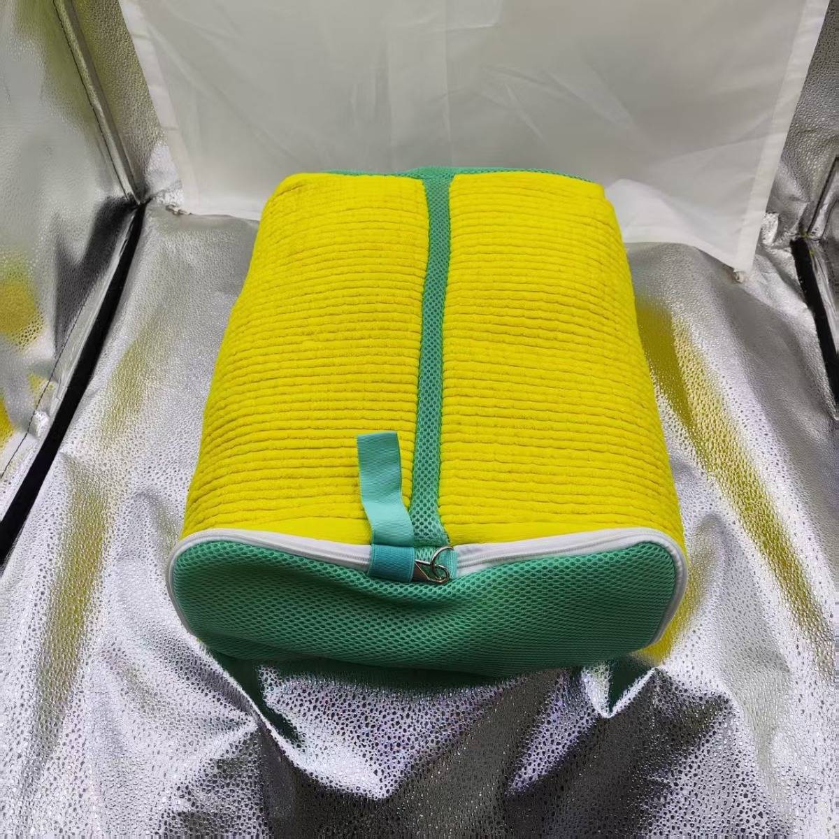 Gelbe zylindrische isolierte Tasche mit grünem Rand und Reißverschluss, die in einer reflektierenden isolierten Versandkühlbox ruht.