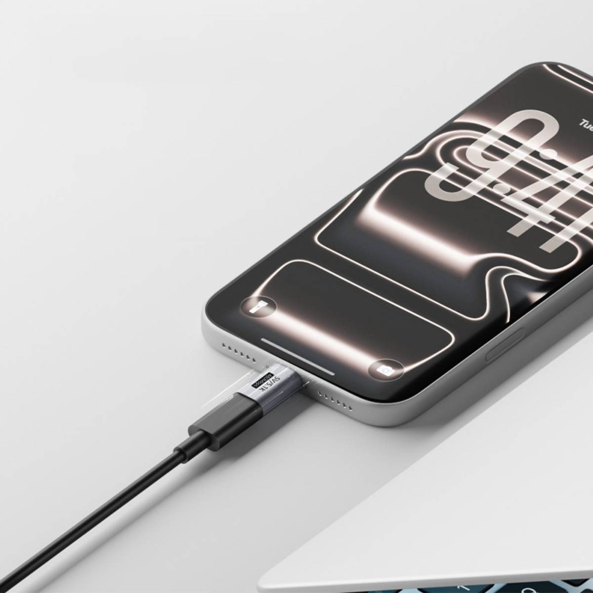 Ein Smartphone, das mit einem Ladekabel verbunden ist, zeigt eine leuchtende Akku-/Ladefläche auf dem Bildschirm an, während es neben einer Laptop-Kante ruht.