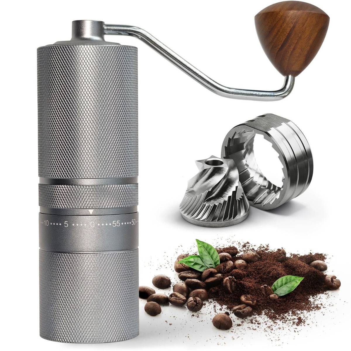 Manuelle Kaffeemühle mit Kurbel, abnehmbaren Mahlwerken, Kaffeebohnen, Kaffeepulver und grünen Blättern auf weißem Hintergrund.